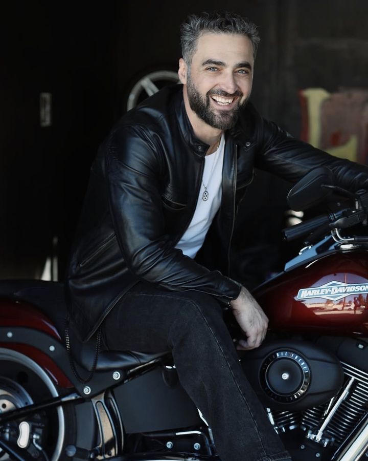 Bacho, co-founder of B.B. Custom, seated on a burgundy motorcycle in the shop